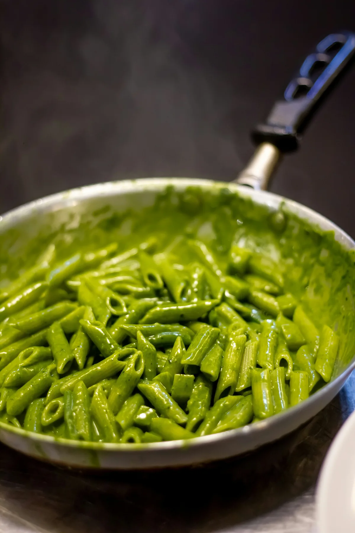 Green penne coated in pesto Genovese in a pan